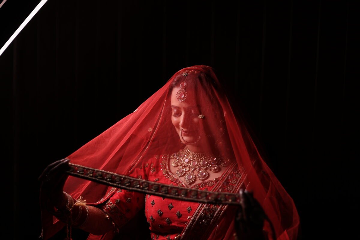 Close up wedding portrait of an Indian bride smiling under a red veil