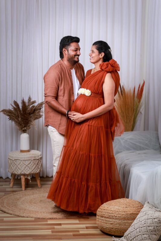 Maternity photoshoot couple in red dress holding baby bump – Make Your Moment Photography Delhi NCR