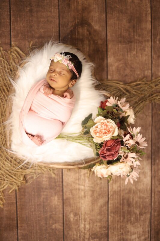 Creative newborn baby photography in Noida with wooden backdrop and floral setup by Make Your Moment Photography