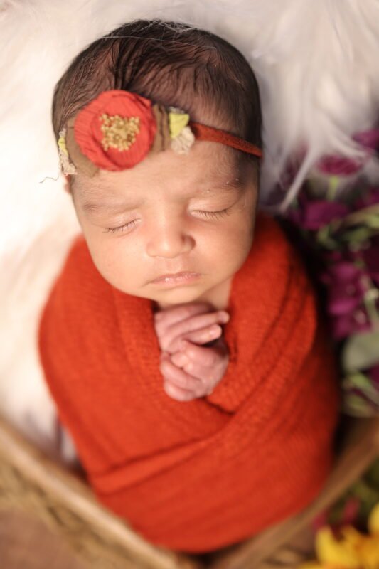 Cute newborn baby photography in Noida with red wrap and floral headband by Make Your Moment Photography