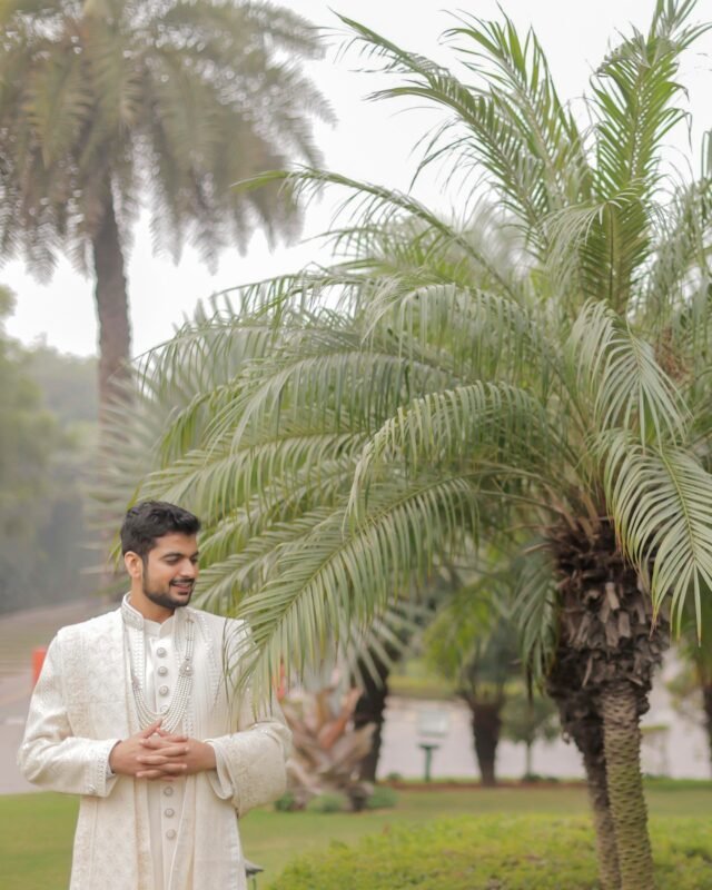 Indian groom standing near palm trees.